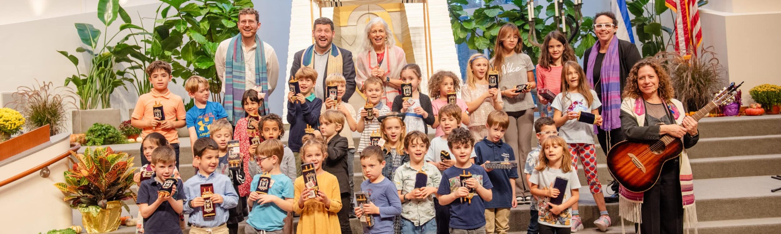 Clergy with a large group of young children holding miniature Torahs