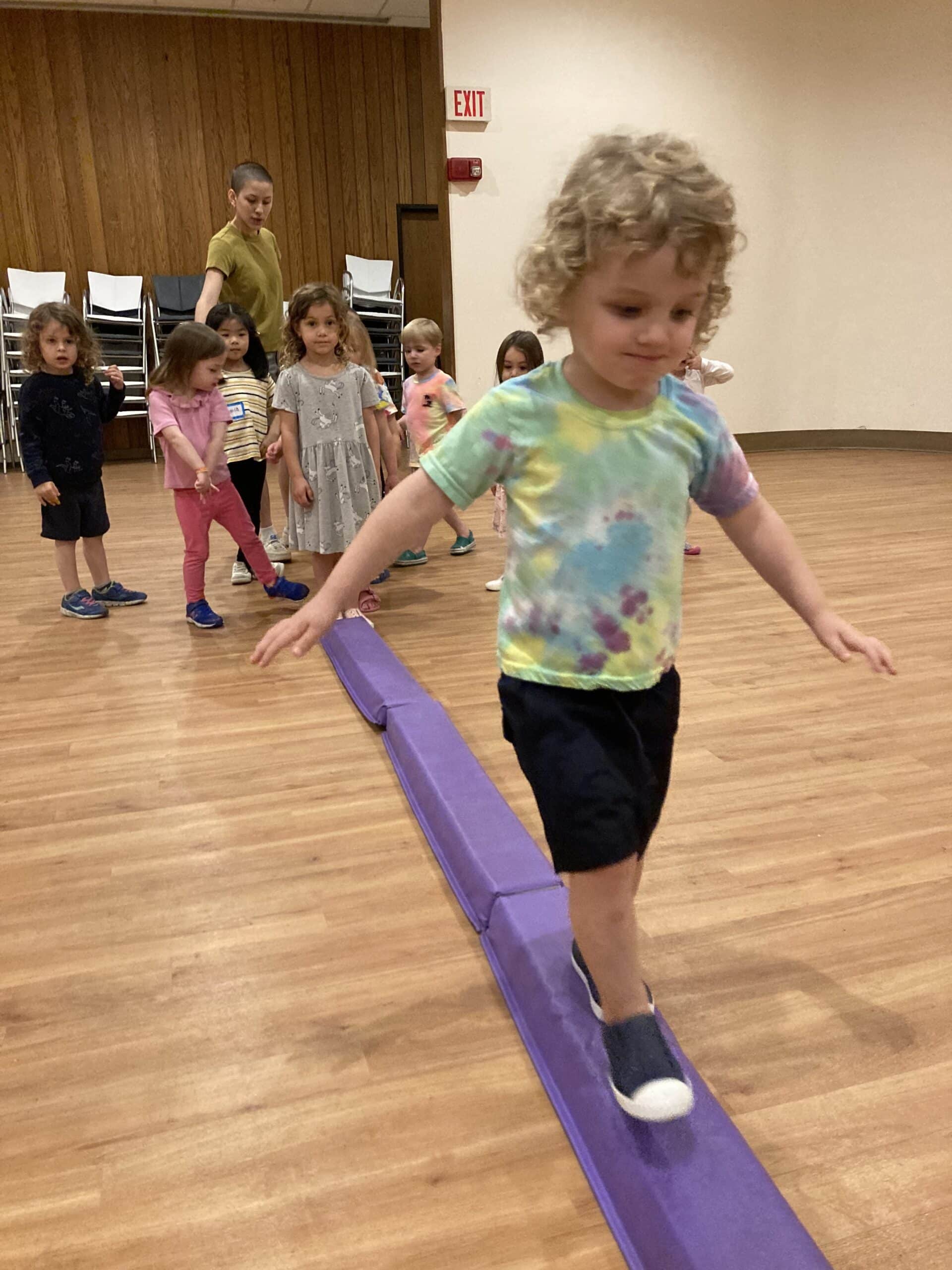 A young boy walking the balance beam with others waiting their turn.