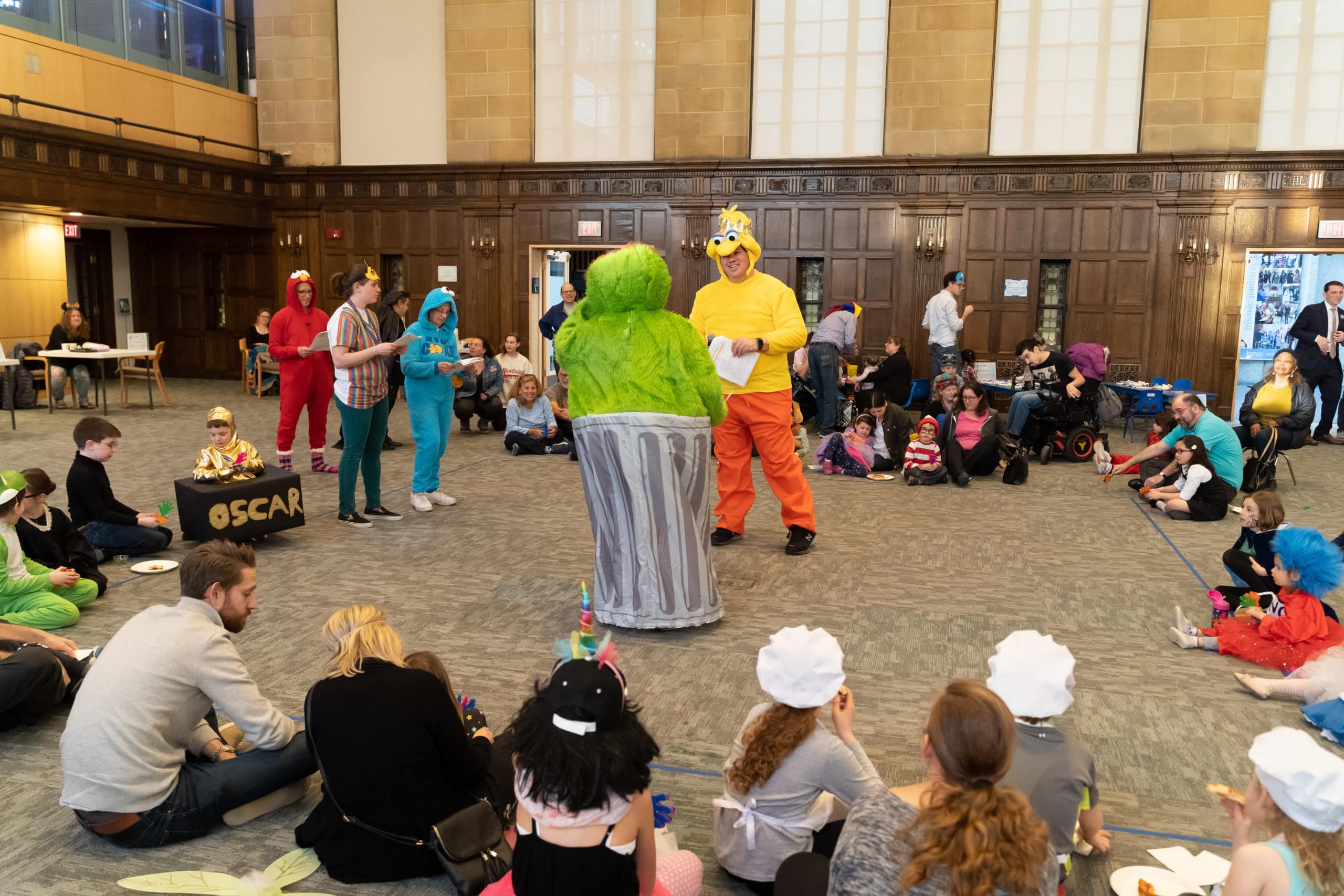 Family Purim celebration at Temple Israel with children in costumes seated in a circle and TI staff performing a skit wearing Sesame Street costumes
