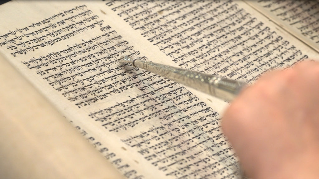 A Torah with a hand holding a pointer as the text is read